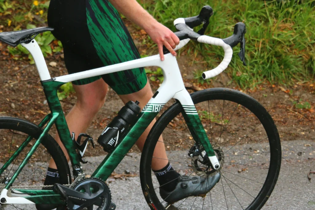 Wielrenner die naast zijn fiets loopt op nat asfalt.